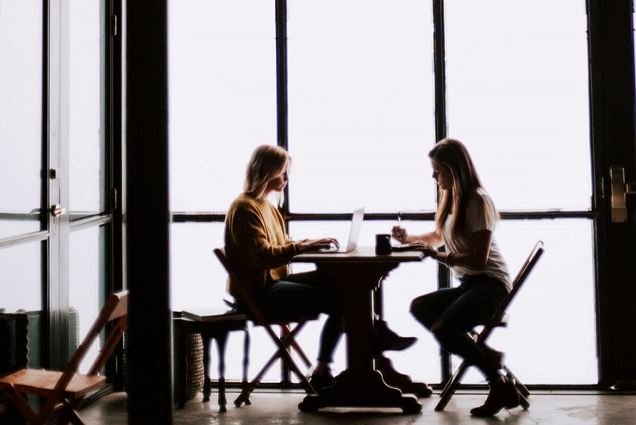 Zwei junge Frauen sitzen an einem Tisch und arbeiten zusammen