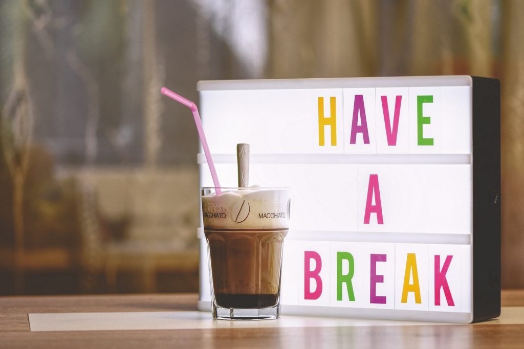 Ein Latte Macchiato steht vor einem Schild das zu einer Ruhezeit während der Arbeitszeit aufruft mit dem Text: Have a Break